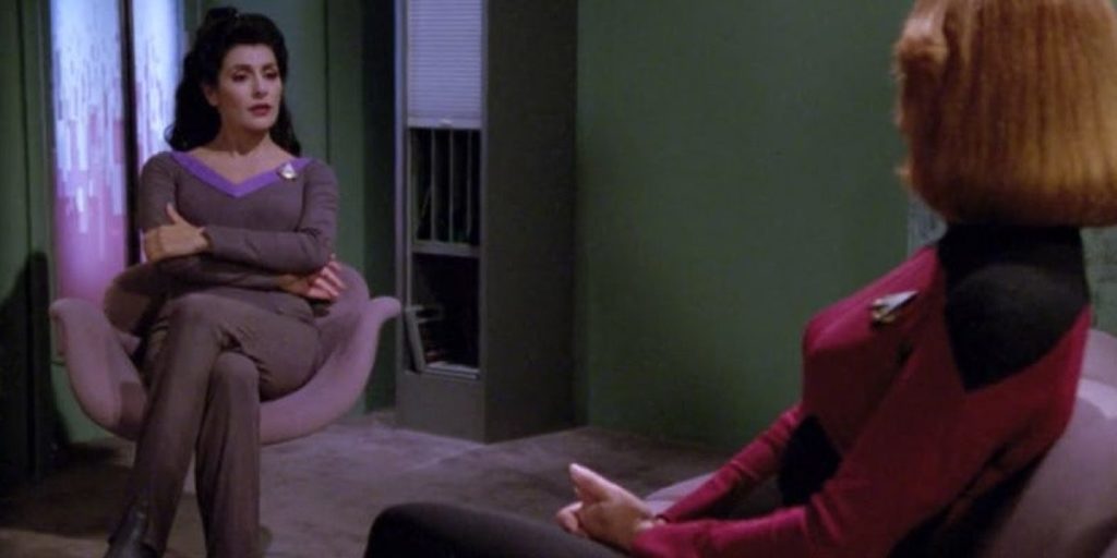 Counselor Troi talks with a member of the Enterprise-D crew while in her office